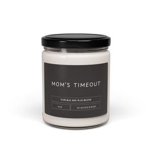 May include: A white candle jar with a black label that reads "MOM'S TIMEOUT" and "NATURAL SOY WAX BLEND". The label also includes the text "9 OZ" and "50-60 HOUR BURN".