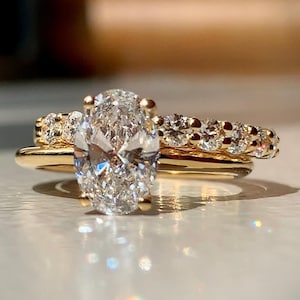 Op de afbeelding: Een gouden ringenset bestaande uit een ring met een grote ovaal geslepen middensteen en een bijpassende ring bezet met een rij kleine, rond geslepen stenen. Het metaal is gepolijst geelgoud en de heldere, gefacetteerde stenen schitteren.