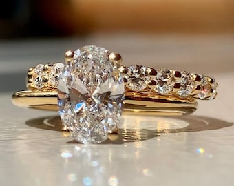 May include: A gold engagement ring set with a large oval-shaped diamond and a matching band of smaller diamonds.