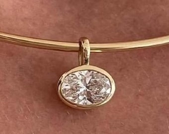 May include: A gold choker necklace featuring an oval pendant with a sparkling gemstone. The pendant is set in a gold bezel. The necklace is a simple, elegant piece of jewellery. The pendant is likely a diamond.