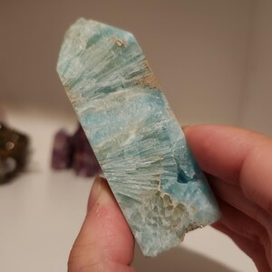 May include: A light blue aquamarine crystal point with a rough, textured surface. The crystal has a pointed tip and a flat base.