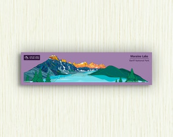 Puede incluir: Una ilustración de Moraine Lake en el Parque Nacional Banff, Canadá. El lago está rodeado de montañas y árboles. El texto "Moraine Lake" y "Banff National Park" está impreso en blanco.