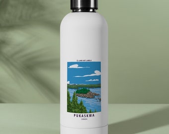 May include: A white water bottle with a black screw-top lid featuring a rectangular graphic label. The label depicts a blue lake, green pine trees, and a rocky island under a blue sky with white clouds, labelled LAND ART LABELS, PUKASKWA, and CANADA.