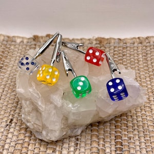 May include: Five colorful dice with white dots, attached to silver clips. The dice are red, yellow, green, blue, and clear with blue dots.
