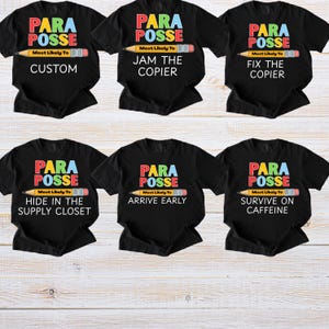 May include: Six black t-shirts with the words "PARA POSSE" in colorful text above a pencil graphic. Each shirt has a different phrase below the pencil: "CUSTOM", "JAM THE COPIER", "FIX THE COPIER", "HIDE IN THE SUPPLY CLOSET", "ARRIVE EARLY", and "SURVIVE ON CAFFEINE".