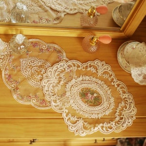 Op de afbeelding: Drie witte kantonderzetters met delicate bloemenborduursels. De onderzetters zijn gerangschikt op een houten oppervlak.