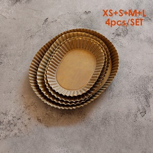 May include: Set of four oval metal trays in different sizes, with a gold finish and a fluted edge. The trays are stacked on top of each other. The text "XS+S+M+L 4pcs/SET" is printed on a white background.
