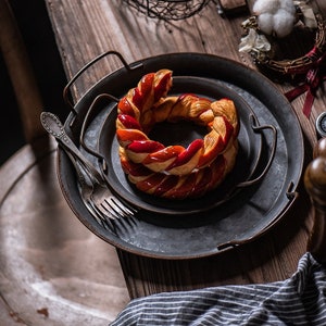Peut inclure: Deux plateaux de service en métal avec une pâtisserie tressée recouverte d'un glaçage rouge au centre. Les plateaux ont un aspect rustique et vieilli.