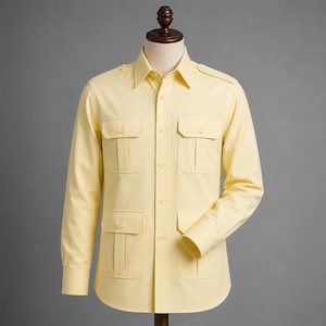 May include: A pale yellow long-sleeved shirt with four front pockets and a collared neckline. The shirt is button-down and has epaulets on the shoulders. The shirt is displayed on a mannequin against a grey background.