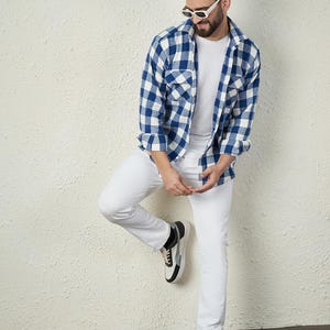 Könnte beinhalten: Ein Mann trägt ein weißes T-Shirt, ein blau-weiß kariertes Flanellhemd, eine weiße Jeans und schwarz-weiße Sneaker.