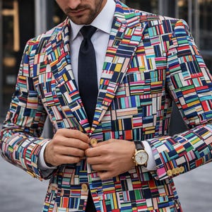 May include: A colorful blazer with a geometric pattern in shades of blue, red, yellow, and green. The blazer is worn over a white dress shirt and a black tie. A gold watch with a black leather band is visible.