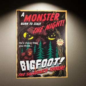 May include: A vintage-style Bigfoot poster with a dark, ominous design. The poster features the text "A Monster Born to Stalk the Night!" and "Bigfoot! The Sasquatch Terror!" with a depiction of the creature and pine trees.