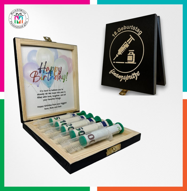 May include: A wooden gift box with a hinged lid, containing syringes filled with rolled-up currency. The box has a printed birthday message and a separate black sign with German text and a syringe graphic. The syringes have green plungers.
