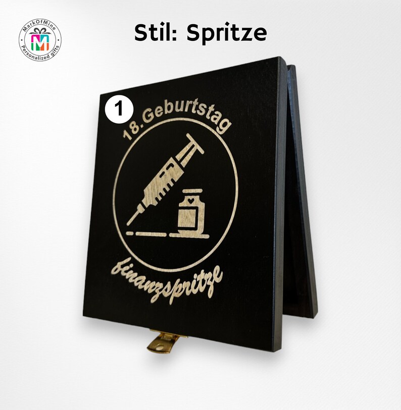 May include: A black wooden sign with a hinged stand. The sign features a circular design with a syringe and vial, and the text "18. Geburtstag finanzspritze". The sign also has the text "Stil: Spritze".