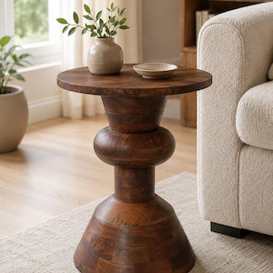 Op de afbeelding: Een donkerbruine houten bijzettafel met een rond blad en een sculpturale, gelaagde voet. De tafel heeft een gladde, gepolijste afwerking met zichtbare houtnerven en staat op een brede, uitlopende basis die naar een centrale kolom toeloopt.