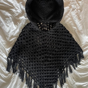 Puede incluir: Poncho de ganchillo negro con capucha, diseño de cuernos de diablo y ribete de flecos.