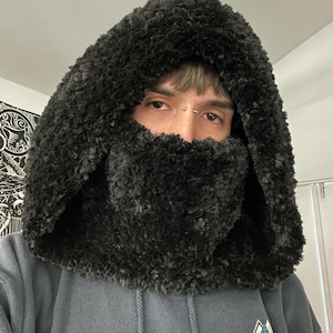 May include: A black hooded sweatshirt with a fuzzy lining. The hood is pulled up over the head and the sweatshirt has a Santa Cruz logo on the front.