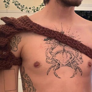 Può includere: Un'epaulette marrone all'uncinetto con dettagli a strati e appuntiti. Il cinturino si estende sul petto. L'articolo è fatto a mano e sembra far parte di un costume o di un ensemble cosplay.