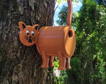 May include: A brown cat-shaped birdhouse is mounted on a tree trunk. The birdhouse features a surprised cat face on one end and a raised tail. The design is whimsical and adds a playful touch to outdoor decor.