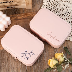 May include: Two pink jewelry boxes with personalized names. The box on the left says "Amelia" with a heart symbol. The box on the right says "Sophie".