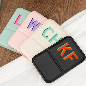 Könnte beinhalten: Vier farbenfrohe Telefonständer mit Buchstaben. Die Ständer sind in Pastellfarben: Mintgrün, Rosa, Creme und Schwarz. Die Buchstaben sind in Kontrastfarben: Pink, Lila, Grün und Orange. Die Ständer liegen auf einem weißen Tuch.