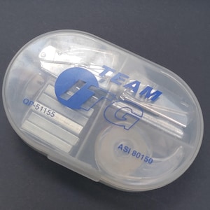 May include: A clear plastic case with a blue and white logo that says "Team TG". The case contains a stapler, staples, a tape dispenser, and a small knife.