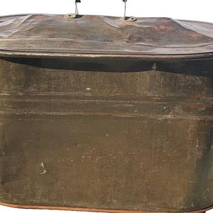 Könnte beinhalten: Eine ovale, antike Metallwanne mit Deckel. Die Wanne hat zwei Griffe an den Seiten und zwei kleine Griffe am Deckel. Das Metall hat ein verwittertes Aussehen mit einer dunklen, bräunlich-bronzenen Farbe.