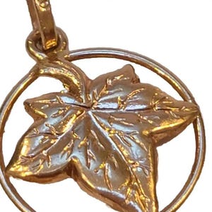 May include: A gold-toned pendant charm featuring a detailed ivy leaf design. The leaf is surrounded by a circular frame.