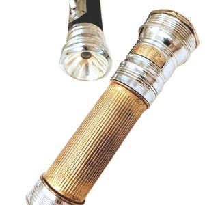 Pode incluir: Duas lanternas vintage. Uma é preta com cabeça prateada e interruptor. A outra é dourada com corpo canelado e detalhes prateados. As lanternas são provavelmente de meados do século XX.