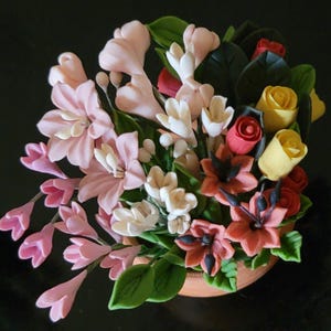 May include: A bouquet of artificial flowers in a terracotta pot. The bouquet includes pink, white, and red flowers, as well as green leaves.