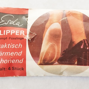 May include: A red and white package with the text "Erda Slipper Strumpf-Füßlinge praktisch wärmend schonend Inhalt: 4 Stück" and a photo of a woman's legs wearing black heels and a pair of white slipper socks.
