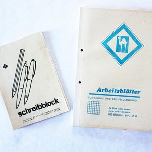 Könnte beinhalten: Zwei Papierprodukte, eines ist ein Schreibblock mit einer Schwarzweißillustration eines Bleistifts und zweier Stifte und dem Text "schreibblock". Das andere ist ein blauer und weißer Ordner mit dem Text "Arbeitsblätter" und "FUR SCHULE UND BERUFSAUSBILDUNG".