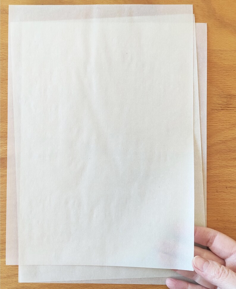 Puede incluir: Dos hojas de papel pergamino blanco, apiladas una encima de la otra, sobre una superficie de madera.