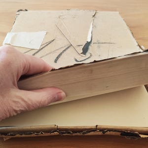 Puede incluir: Un libro vintage con una cubierta de cart&oacute;n marr&oacute;n y un interior de papel blanco. El libro est&aacute; ligeramente da&ntilde;ado y tiene un trozo de cinta adhesiva en la cubierta.