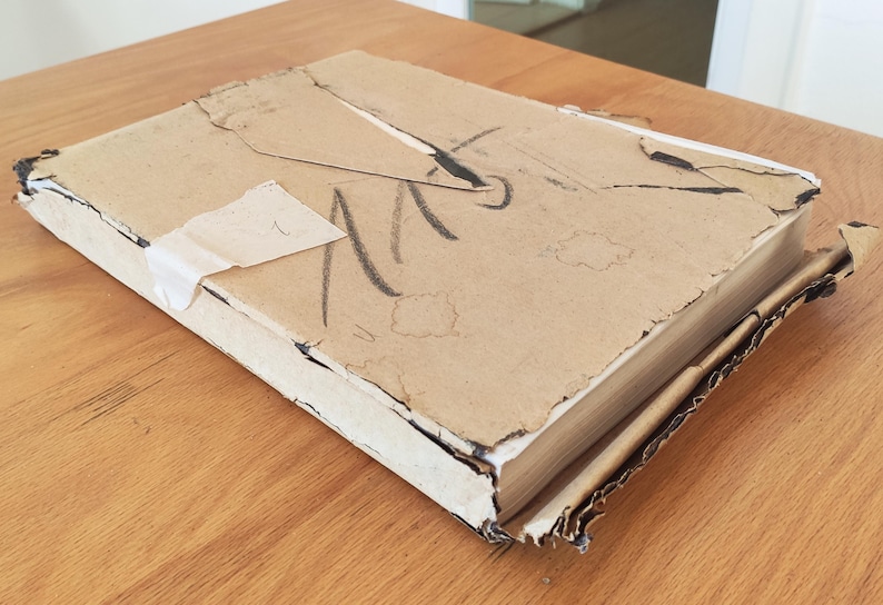 Puede incluir: Una caja de cart&oacute;n desgastada con una etiqueta blanca y marcas negras. La caja est&aacute; ligeramente da&ntilde;ada y tiene un aspecto desgastado y envejecido.