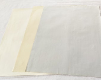 May include: Three sheets of paper in different shades of white, cream, and light gray. The sheets are arranged in a row from left to right, with the lightest sheet on the left and the darkest sheet on the right.