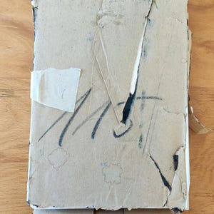 Puede incluir: Una caja de cart&oacute;n desgastada con marcas negras y cinta adhesiva. La caja est&aacute; ligeramente da&ntilde;ada y tiene algunas manchas marrones.