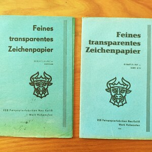 Peut inclure: Deux blocs de papier bleu turquoise avec le texte "Feines transparentes Zeichenpapier" et une illustration de taureau. Chaque bloc contient 25 feuilles, mesurant 21 x 29,7 cm. Le bas des blocs indique "VEB Feinpapierfabriken Neu Kolib Werk Hohenofen".