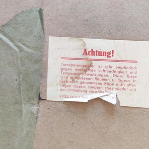 Puede incluir: Una tarjeta blanca con la palabra "Achtung!" en letras rojas. La tarjeta tiene texto en alem&aacute;n sobre el cuidado del papel transparente. El texto dice: "Transparentpapier ist sehr empfindlich gegen wechselnde Luftfeuchtigkeit und Temperaturschwankungen. Diese Riese sind in trockenen R&auml;umen zu lagern. In Gebrauch genommene Riese nicht offen liegen lassen, sondern stets wieder mit der Umh&uuml;llung verschlie&szlig;en. SVZL IL-10-7 DIG 107"