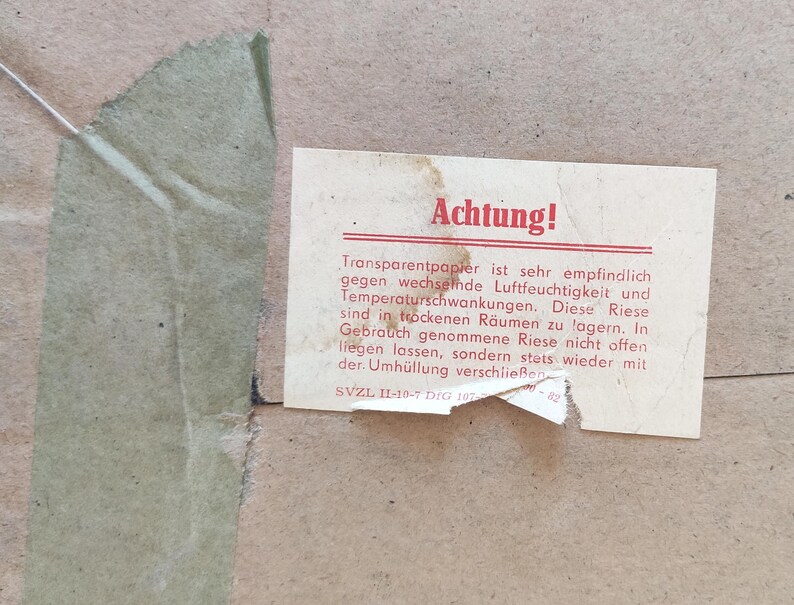 Puede incluir: Una tarjeta blanca con la palabra "Achtung!" en letras rojas. La tarjeta tiene texto en alem&aacute;n sobre el cuidado del papel transparente. El texto dice: "Transparentpapier ist sehr empfindlich gegen wechselnde Luftfeuchtigkeit und Temperaturschwankungen. Diese Riese sind in trockenen R&auml;umen zu lagern. In Gebrauch genommene Riese nicht offen liegen lassen, sondern stets wieder mit der Umh&uuml;llung verschlie&szlig;en. SVZL IL-10-7 DIG 107"