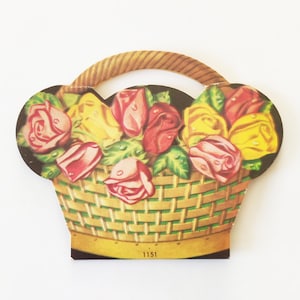 May include: A vintage paper craft of a basket filled with red, yellow, and pink roses. The basket has a brown woven handle and the number 1151 is printed on the bottom.