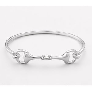 Op de afbeelding: Een zilverkleurige armband met een paardenbit-ontwerp. De armband heeft een cirkelvormige band met een centraal paardenbit-ornament, met paardensport-geïnspireerde sieraden.