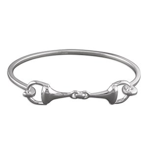 May include: A silver bangle bracelet with a horse bit design. The bracelet is made of polished metal and has a simple, elegant look.