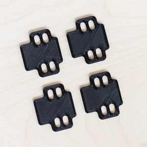 Op de afbeelding: Vier zwarte kunststof onderdelen met meerdere gaten, mogelijk voor een 3D-printer.