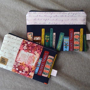 Könnte beinhalten: Zwei Stoff-Reißverschlusstaschen. Eine hat einen marineblauen Hintergrund mit farbenfrohen Buchrücken, darunter "Gullivers Reisen" und "Peter Pan". Die andere hat ein Blumenmuster und den Text "100% Einzel Stück".