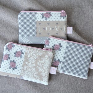 Könnte beinhalten: Drei kleine Reißverschlusstaschen mit Patchwork-Designs. Die Taschen weisen eine Mischung aus Mustern auf, darunter Vichy, Blumen und ein Feld mit dem Wort "LOVE". Die Farbpalette umfasst Grau, Rosa und Creme.