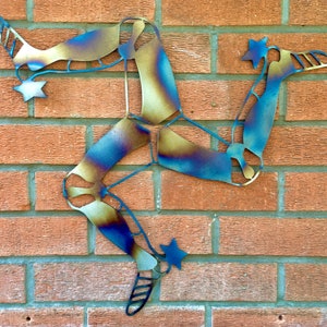 May include: A metal sculpture of the three legs of Mann, a symbol of the Isle of Man. The sculpture is made of metal and has a blue and gold finish.