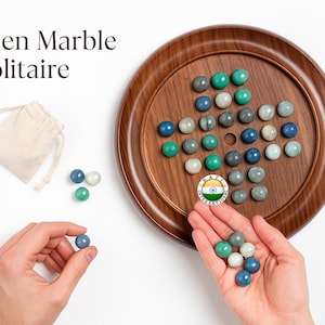 May include: Wooden Marble Solitaire game with a wooden board and colorful marbles. The game includes a drawstring bag and is played with a set of marbles in various shades of blue, green, and white. The game board is round and has a dark brown finish.