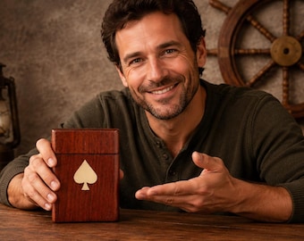 May include: A wooden playing card box with a spade symbol. The box is a rich, dark brown color and appears to be made of wood. The spade symbol is a lighter color, possibly gold or cream. The box is rectangular and appears to be closed.