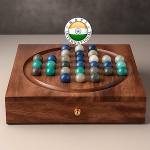 May include: A wooden solitaire game with a square base and a circular playing field. The game includes a set of colorful marbles in shades of blue, green, gray, and white. The wooden box has a small gold-colored knob.